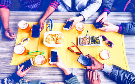 Group of friends texting phone message inside pub top view image - Multicultural teenagers social network addicted together around table with pints of beer and snacksの写真素材