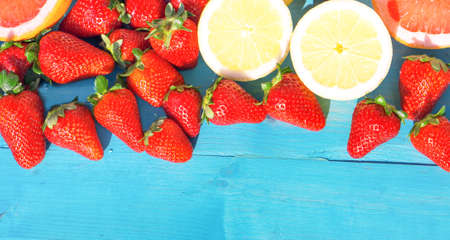 Strawberries and sliced lemons on aquamarine wooden table background with horizontal space to add text - Top view of fresh fruits of spring seasonの写真素材