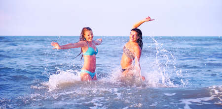 Young women playful bathing summer moments on the beach at sunset - Happy carefree girls open arms having fun in blue ocean playing with water splashes on tropical vacation - Female freedom conceptの写真素材