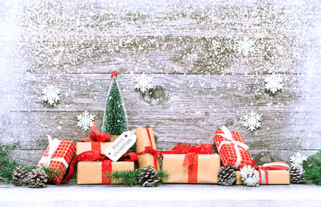 Christmas gift boxes with snowfall on wooden background - Winter holidays wrapped presents composition with pinecones fir tree branch and falling snow - Seasonal concept of decoration and festivityの写真素材