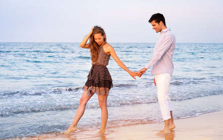 Young couple walking at sunset on the beach - Happy lovers holding hands relaxing by the ocean -  Romantic concept of holidays in hot countries - Main focus on womanの写真素材