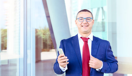 Confident business man smiling looking at camera and holding mobile phone - Well dressed manager...