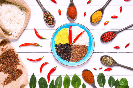 Different types of rice  surrounded by variety of aromatic spices top view image on white wood...