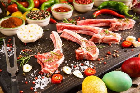 Raw lamb ribs preparation on rustic cutting board - Fresh chops of meat with colorful spices and vegetables background - Easter holidays food conceptの写真素材