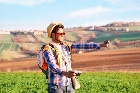 Happy indian hiker taking selfie using phone and old camera on fields background at sunset lights - Young asian tourist holding mobile standing in cultivated countryside - World travel concept - imageの写真素材