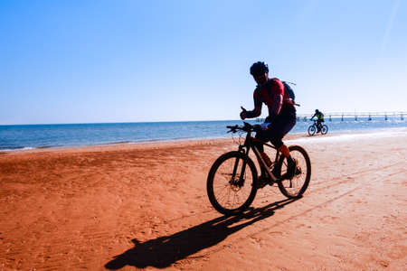Man cycling on sport bike showing thumb up on ocean background - Silhouette of people riding bicycle on the beach shore with morning backlight - Lifestyle concept of healthy holiday activity - imageの写真素材