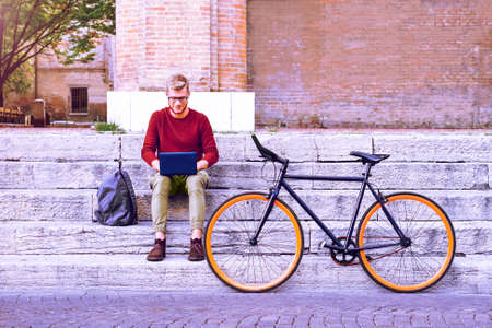 Commuter man with laptop and sport bike sitting on old city steps - University student using notebook - Young freelance guy works on computer outdoor - Concept of modern technology , job opportunitiesの写真素材