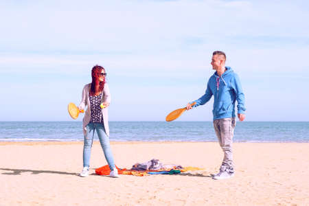 Couple playing beach tennis game on the sand with blue ocean and sky background - Playful young friends having fun with healthy recreation on summer holiday - Travel concept of  joyful moment - Imageの写真素材