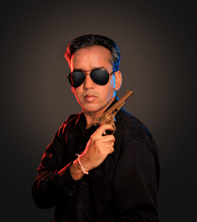Indian Man with sunglasses and gun on dark background