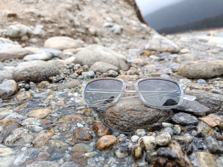 A pair of modern, stylish, and trendy sunglasses or shades or sunnies placed on the top of a rock in a stream of water with beautiful natural background. The sunglasses have grey tinted lensesの写真素材