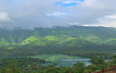Panoramic landscape view of beautiful lush green Sahyadri mountains range in monsoon with windmills visible through clouds on the top at Tapola, a famous tourist destination in Maharashtra, Indiaの写真素材