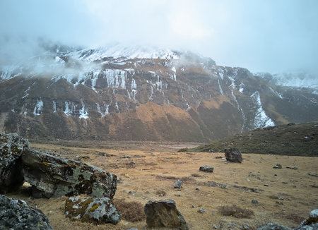Panoramic landscape view of beautiful snowcapped great Himalayas with frozen waterfalls on a foggy winter day in North Sikkim. There are large boulders and hay. They are famous for tourism in India.の写真素材
