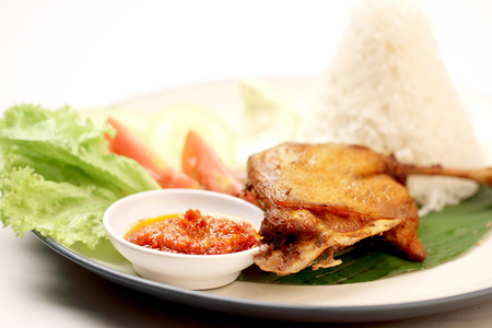 Indonesian Traditional Fried Chicken with Rice, Sambal, and Vegetables on a White Plateの写真素材