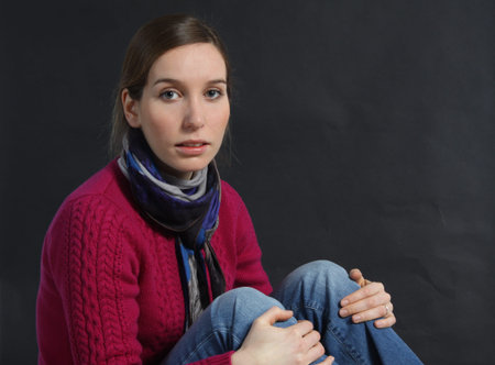 Beautiful, young brunette wearing a maroon colored sweater against a dark back-ground,