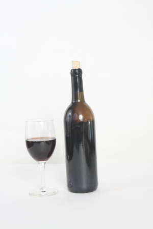 Bottle and glass of red wine against a light colored background. の写真素材