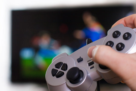 hand holding silver gamepad on a front of big screen with soccer game
