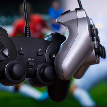 black and silver gamepads close up with soccer game on background