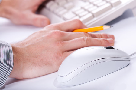 mans's hands working on a office place with all white computer devices