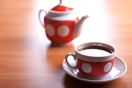 cup of black tea close up on a table with teapot blurred on backgroundの写真素材