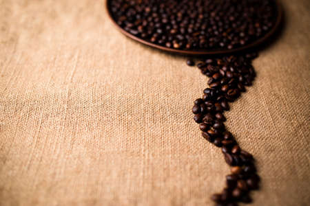 scattered beans of coffee on the tablecloth and plate of beans in the backgroundの写真素材