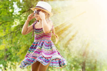 happy little girl in colorfull dress and hat twissting around cat summer dayの写真素材