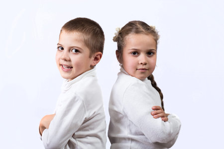 Cute brother and sister standing back to back, like they are in quarrel on a white backgroundの写真素材