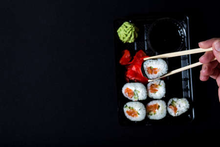Delivery sushi service. Set of sushi in plastic box on black background. picking of roll from box with sushi.の写真素材