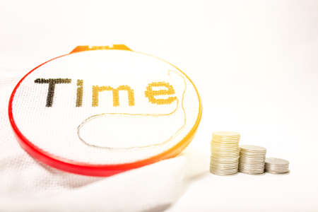 The concept of the value of time spent. The word time is embroidered in black beads on a white background with a stack of coins on a white background.の写真素材