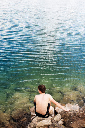 A man swims in the crystal clear water of a lake with a rocky shoreの写真素材