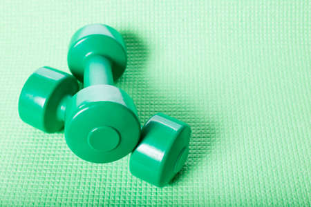 Green dumbbells on green fitnes mat with copy space.の写真素材