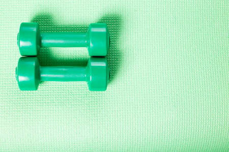Green little dumbbells on green fitnes mat with copy space.の写真素材