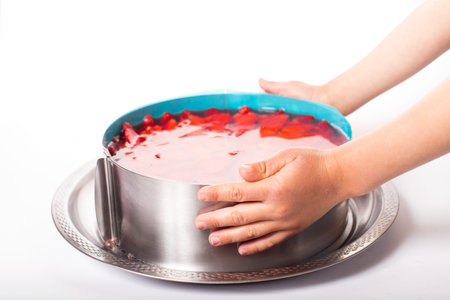 Children hands holding strawberry cheesecake in metal form on a white background.