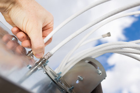 Man's hand connecting Cable to 4G antenna close up with sky on background.