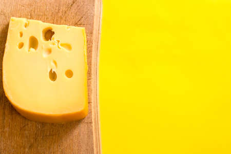 Piece of Maasdam cheese on wooden board, with yellow copy space.の写真素材