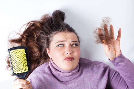 Sad young girl holding clump of loose hair in hand, on a white background.の写真素材