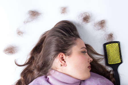 Sad face of girl with clumps of lost hair and hair brush, on a white background.の写真素材