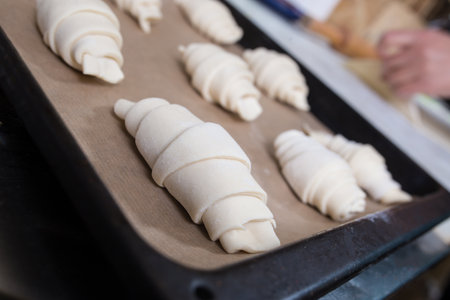 Raw croissants close up in focus, and hands with a rolling pin in the background.の写真素材