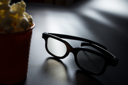 Bucket of popcorn and 3D glasses on black background with copy space.