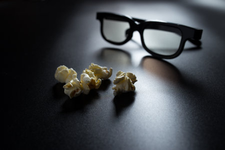 Fzlakes of popcorn close-up on black with 3D glasses blured on background.の写真素材