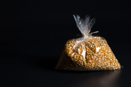 Seeds of popcorn in plastic bag, on blacl background with copyspace.