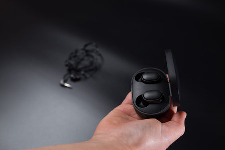 Hand holding black wireless headphones and wired headphones on black background.