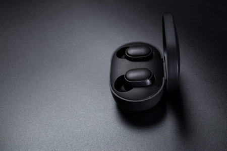Black wireless earphone in charging case, on black background with copyspace.の写真素材