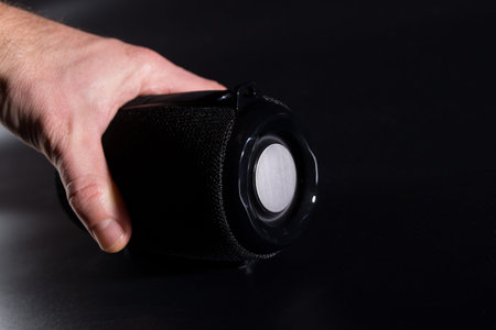Hand holding wireless portable speaker on black background with copy space.