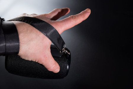 Hand holding on belt black portable wireless speaker, on black background with copyspace.の写真素材