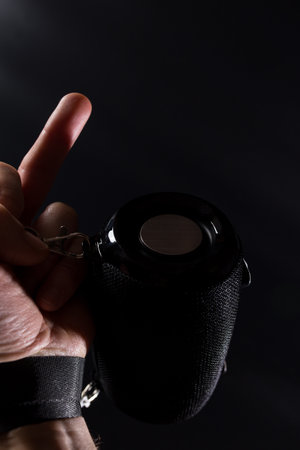 Hand with fuck sign holding black wireless speaker on black background.の写真素材