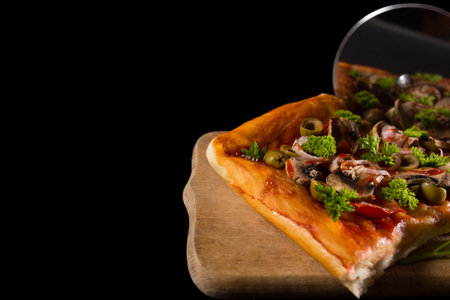 Cuting pizza withroller knife on kitchen board, on black background with copyspace.の写真素材