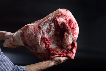 Butcher holding pork thigh in hands on black background.