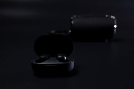 Black wireless headphones in charging case on black with wireless speaker on background.の写真素材