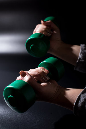 Female hands with dumbbells close up having fitness training on black background.