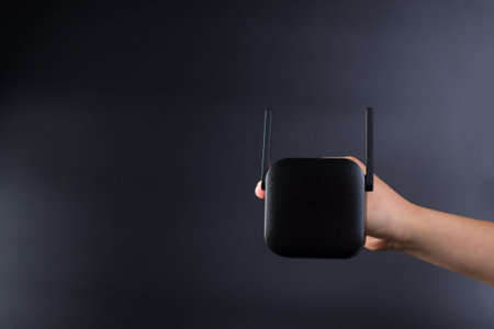 Hand holding black wifi amplifier, on black background with copy space.